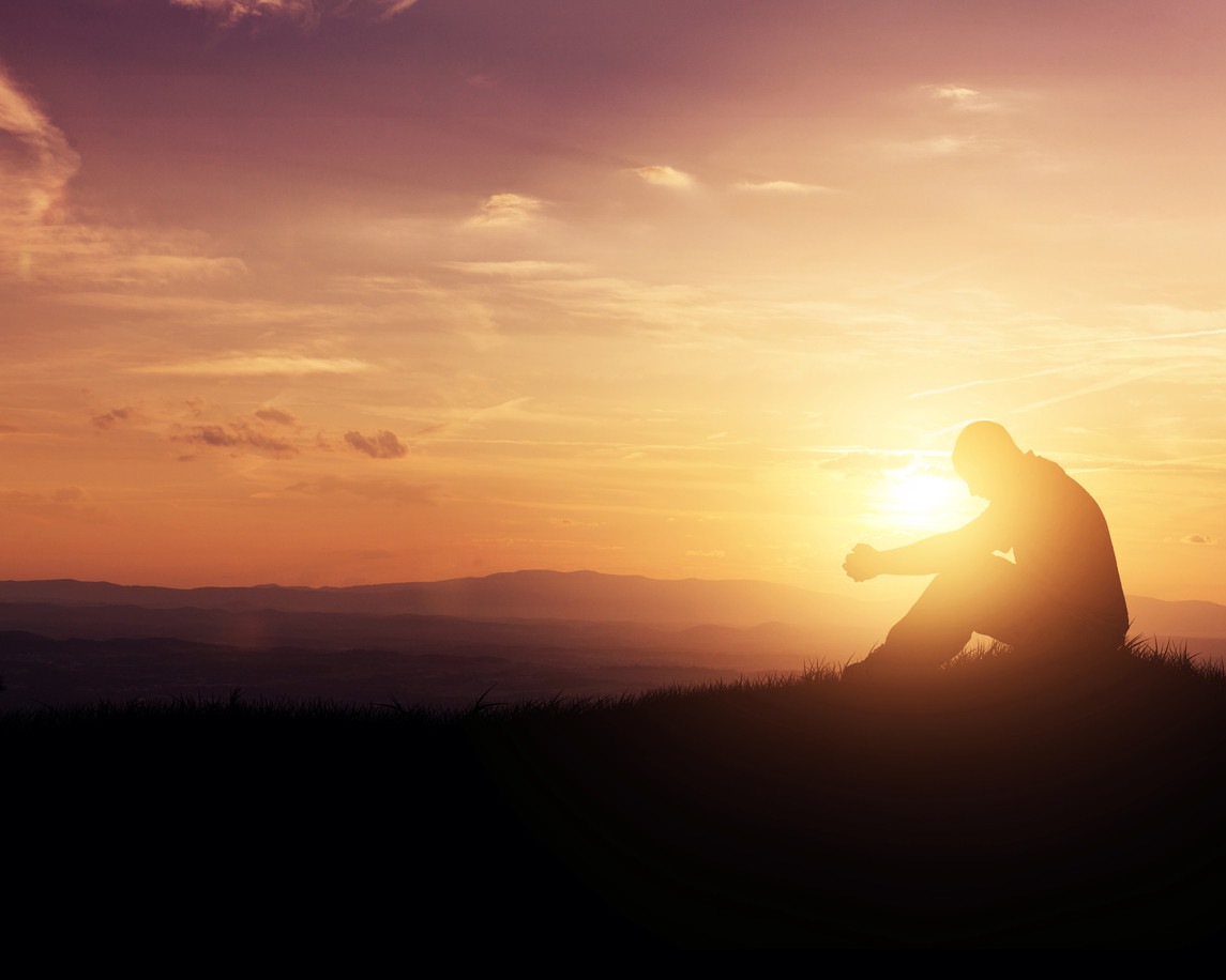 Silueta de una persona sentada contemplando un cielo al atardecer en tonos naranja y púrpura sobre colinas lejanas